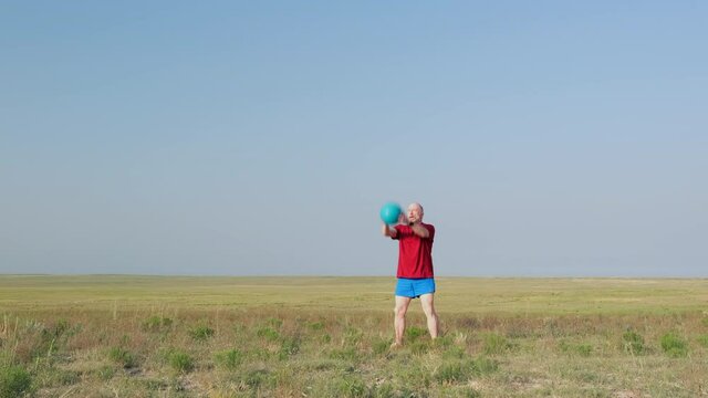 morning workout with a heavy slam ball - senior man is exercising throw-ups in a prairie of Pawnee National Grassland in Colorado