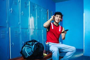 young latin disabled man Paralympic athlete with phone and headphones in the locker room at gym...