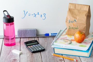 Straight on view of a table top scene of school supplies including lunch bag and water bottle,...