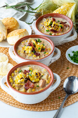 Three soup crocks in a row filled with chicken and corn chowder and garnished with grilled corn, bacon and chives.