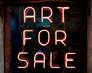 A neon sign announces ART FOR SALE in a store window in Lacoste in the Luberon Valley of France.