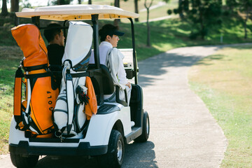 A golfer drives a golf cart down a golf course road while playing a game.
