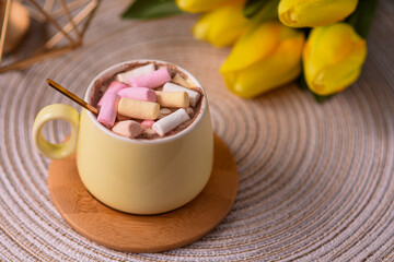 Marshmallows in a coffee cup with a golden teaspoon on a wooden cup holder.