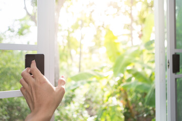 Hand holding open white window with natural blurred background  and sunlight