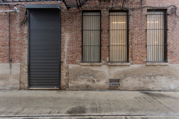 Rolling metal door on back of a vintage brick building with tall windows covered by steel bars