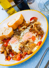 Hearty breakfast of eggs fried with pork meat and sliced tomatoes seasoned with dried herbs served with bread