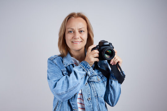 Senior woman photographer with professional photo camera on gray background