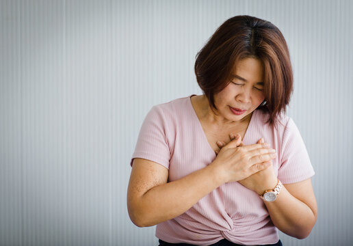 Middle Age Asian Woman Sitting On Bed Suffering From Sudden Heart Attack And Hold Chest. Concept Of Emergency Health Care And Affected From  Cardiopulmonary Resuscitation, Heart Problem