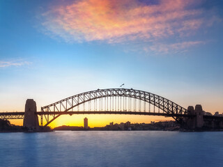 Long exposure view of Sydney Harbour Bridge on a beautiful day at Sunset with North Sydney skyline silhouetted behind in Australia.