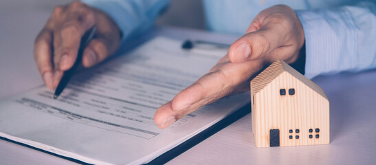 Real estate agent holding home and signing contract about agreement of real property on desk, house...