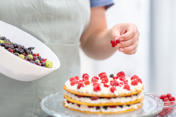 Chef hands spread fresh raspberries on a cheese cream cake