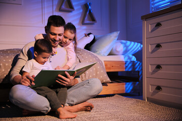 Father reading bedtime story to his children at home - obrazy, fototapety, plakaty