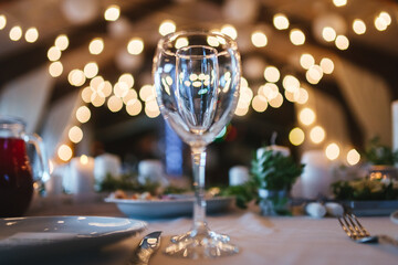 Two glasses for wine and champagne are on table on white tablecloth against background of blurred warm lights. Concept of celebrating any event with alcohol. Illusion of one glass in another