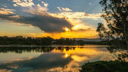 Fototapeta premium Landscape spectacular golden reflections of the clouds and sunset in the beautiful, calm waters of a broad river in eastern Australia.
