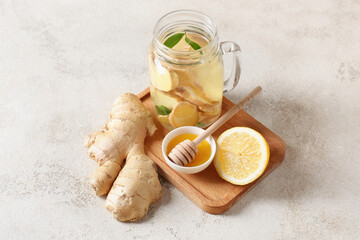 Wooden board with fresh ginger lemonade, honey and lemon on light background