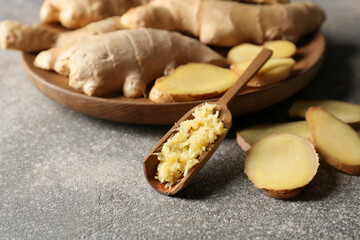 Scoop with fresh grated ginger and slices on dark background