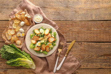 Plate with tasty Caesar salad and sauce on wooden background