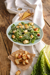 Plate with tasty Caesar salad on wooden background