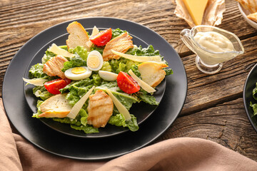 Plate with tasty Caesar salad and sauce on wooden background