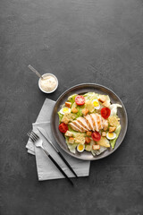 Plate with tasty Caesar salad and sauce on dark background