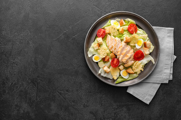 Plate with tasty Caesar salad on dark background