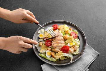 Woman eating tasty Caesar salad on dark background