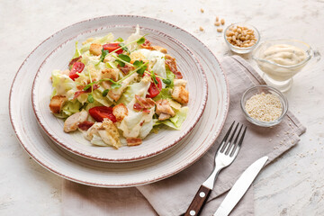 Plate with tasty Caesar salad, pine nuts and sauce on light background