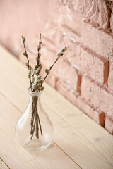 Vase with willow branches on table near color brick wall