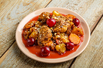 Jewish dish stewed potatoes with chicken in cherry sauce decorated with cherries.
