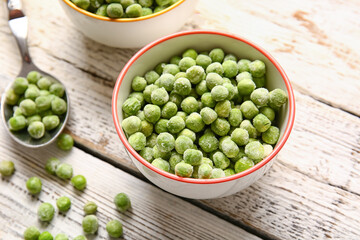 Bowls and spoon with frozen green peas on light wooden background