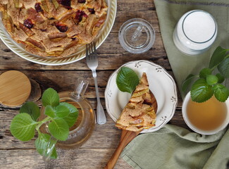 Round large homemade charlotte fruit pie on a wooden ancient natural table with tea, teapot and mint. Apples and plum.Place for text.
