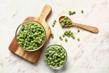 Bowls and spoon with frozen green peas on light background