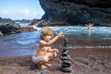 Funny kid boy making stones pyramid on pebble beach symbolizing stability, zen, harmony, balance.