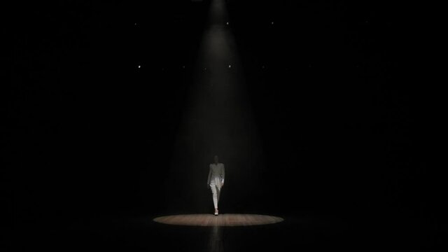 A singer with long hair enters the stage in the light of one white spotlight.