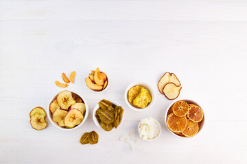 Dried apple, pear, pineapple,kiwi,apricot, coconut, orange and mandarin chips on bowls on grey background. Vegan snack, sugar free food. Top view.