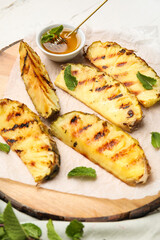 Board with grilled pineapple slices and honey on light wooden background