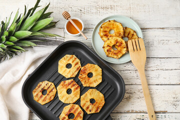 Frying pan with grilled pineapple slices and honey on light wooden background