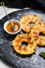 Slate plate with grilled pineapple slices and honey on light background, closeup