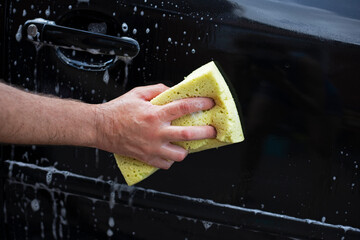 wash the fender of a black car with a washcloth on a sunny day in the garden after a flood,