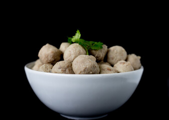 Meatballs noodle are placed in a white cup with cilantro on top. on a black background selective focus