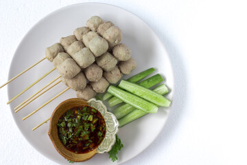 Meatballs on skewers, meatballs, beef noodles with vegetables, and a cup of dipping sauce put on a plate and white background