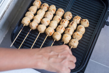 Woman using her hands to cook meatballs on a black grill pan Asian food Thai food.