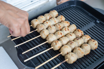Woman using her hands to cook meatballs on a black grill pan Asian food Thai food.