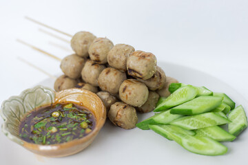Grilled meatballs, skewers, meatballs, noodles with vegetables and dipping sauces burnt on plate and white Asian food.