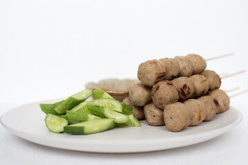 Grilled meatballs, skewers, meatballs, beef noodles with vegetables and dipping sauces burnt on a plate, and white Asian food.