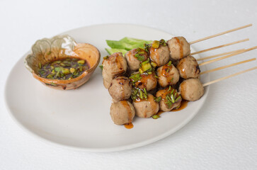 Grilled meatballs, skewers, meatballs, beef noodles with vegetables and dipping sauces burnt on a plate, and white Asian food.