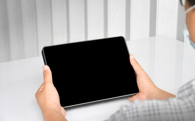 Shoulder view of a young man who holding a black blank screen laptop in hands, concept for monitoring stock market and online learning  at home, soft and selective focus on taplet.