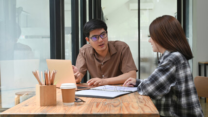 Two young business people discussing their new project together at co working space.