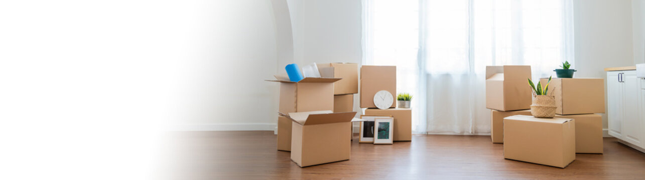 Moving in. Stack of cardboard boxes and household stuff belongings in the white empty apartment room carton with copy space. Lifestyle moving house relocation unpacking background concept banner