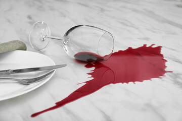 Overturned glass and spilled red wine on white marble table